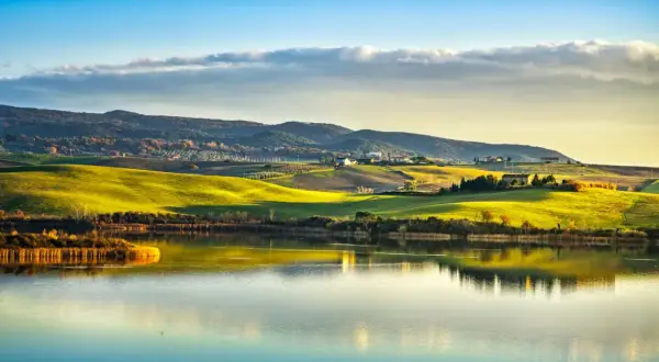 Dolci colline toscane illuminate dal sole al tramonto si specchiano nel lago di Santa Luce, creando un paesaggio incantevole.