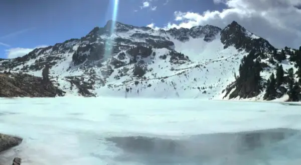 Il lago delle stellune, ghiacciato e circondato da montagne innevate, riflette il cielo azzurro e le nuvole.