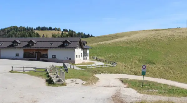 Malga Arpaco, un edificio bianco con tetto scuro, si erge su un prato verde sotto un cielo azzurro.