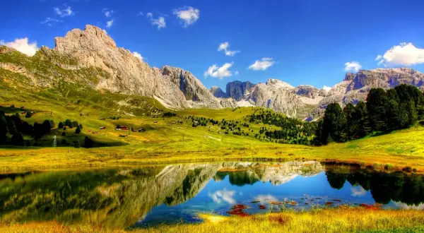 Un lago alpino riflette montagne maestose e prati verdi. Perfetto per le cose da fare in estate: escursioni, relax e ammirare la natura.