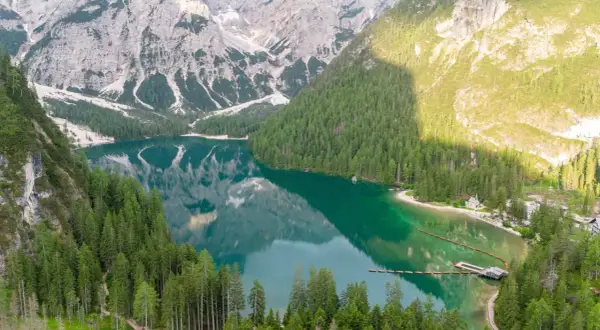 Un lago alpino dalle acque smeraldine, circondato da fitti boschi e montagne imponenti. Un luogo perfetto per le vacanze al lago, con un pontile e un piccolo borgo.