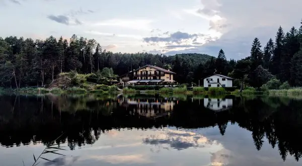 Riflessi serali sul lago di Santa Colomba, con un albergo e una casa immersi nel verde degli alberi.