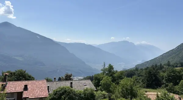 Case con tetti rossi ai piedi del monte Biaina, con valli e montagne azzurre all'orizzonte sotto un cielo limpido.