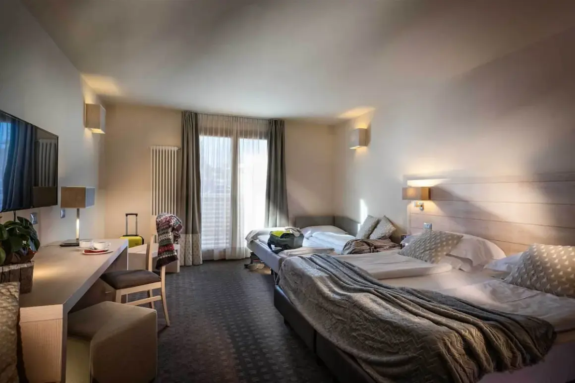 A hotel room with two beds, a desk, and a TV.