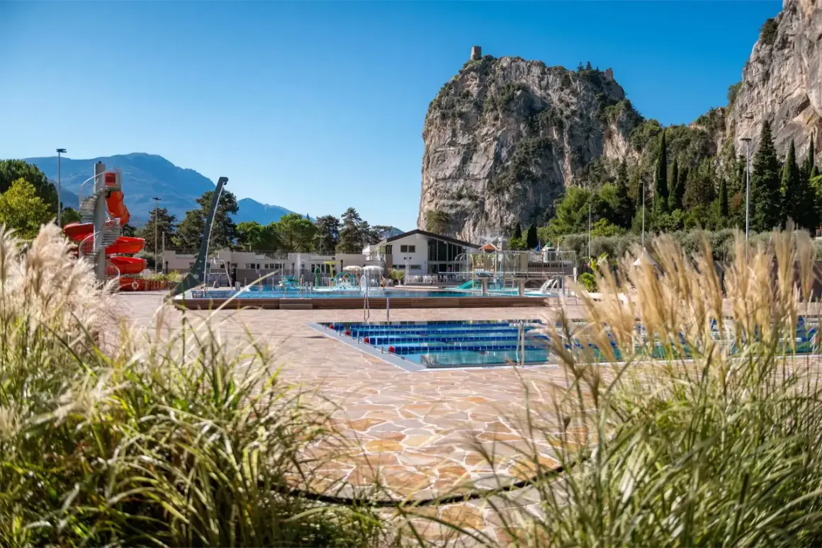 Piscina con scivoli rossi e montagne sullo sfondo, ideale per un soggiorno in campeggio ad Arco.