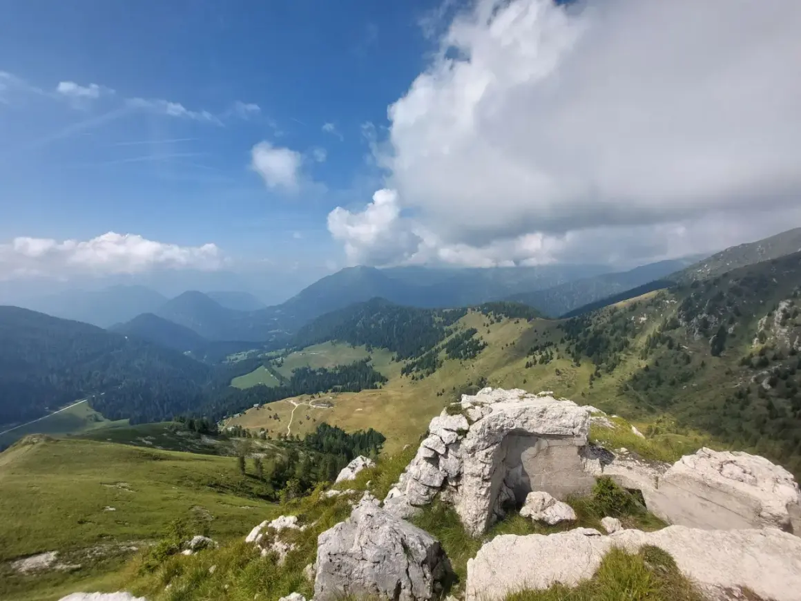 Rovine di un bunker sul **Castello Tesino**, con vista su verdi valli e montagne nebbiose sotto un cielo azzurro e nuvoloso.