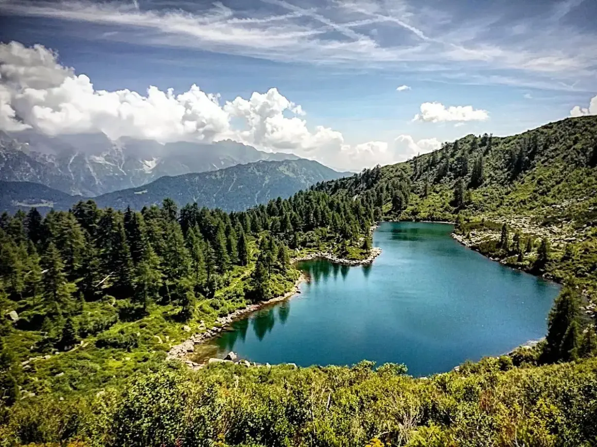 I laghi di San Giuliano, incastonati tra montagne e foreste di conifere, riflettono un cielo azzurro con nuvole bianche.