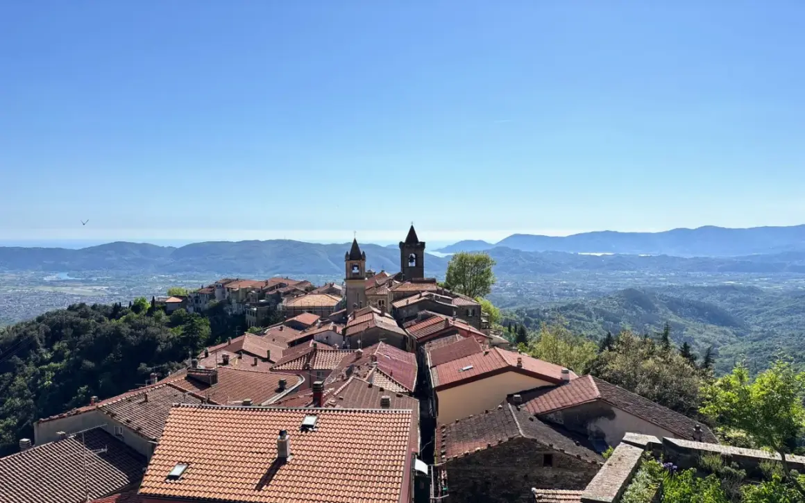 Panoramica di un borgo collinare con tetti rossi e campanili, che rivela dove si trova Fosdinovo, con il mare e le montagne all'orizzonte.