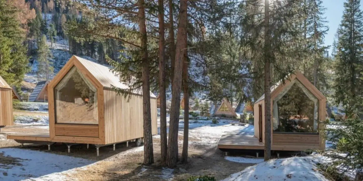 Piccole case in legno con grandi vetrate, immerse in un bosco innevato. Un'oasi di pace per alloggi particolari.