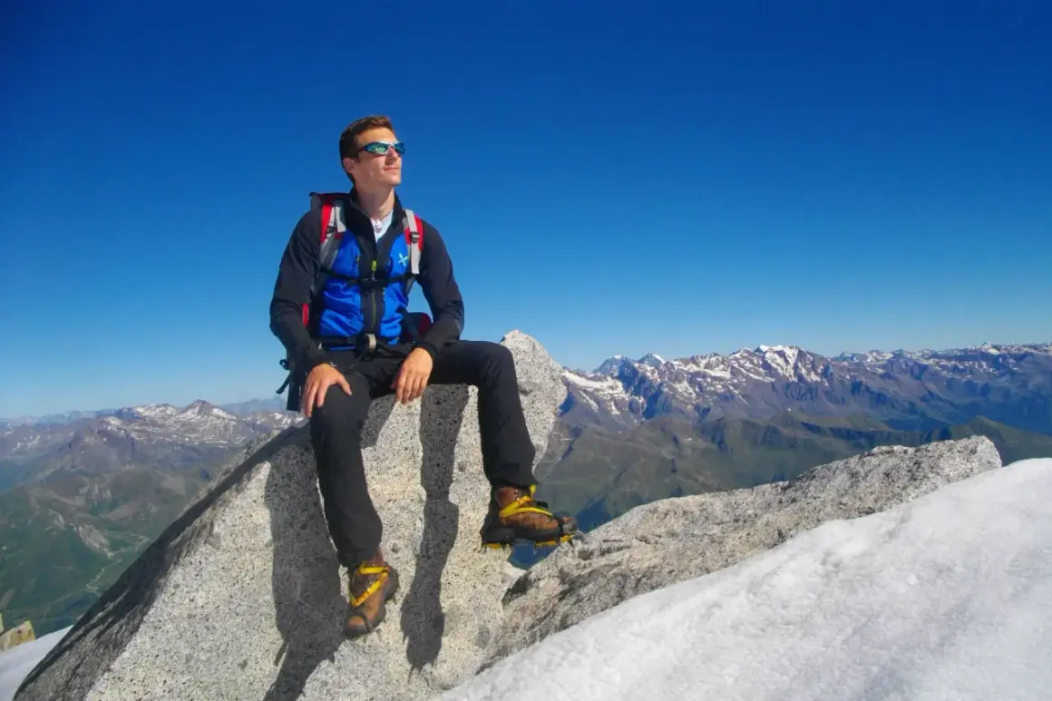 Giovane alpinista seduto sulla cima Presanella, ammira il panorama mozzafiato delle Alpi sotto un cielo azzurro.