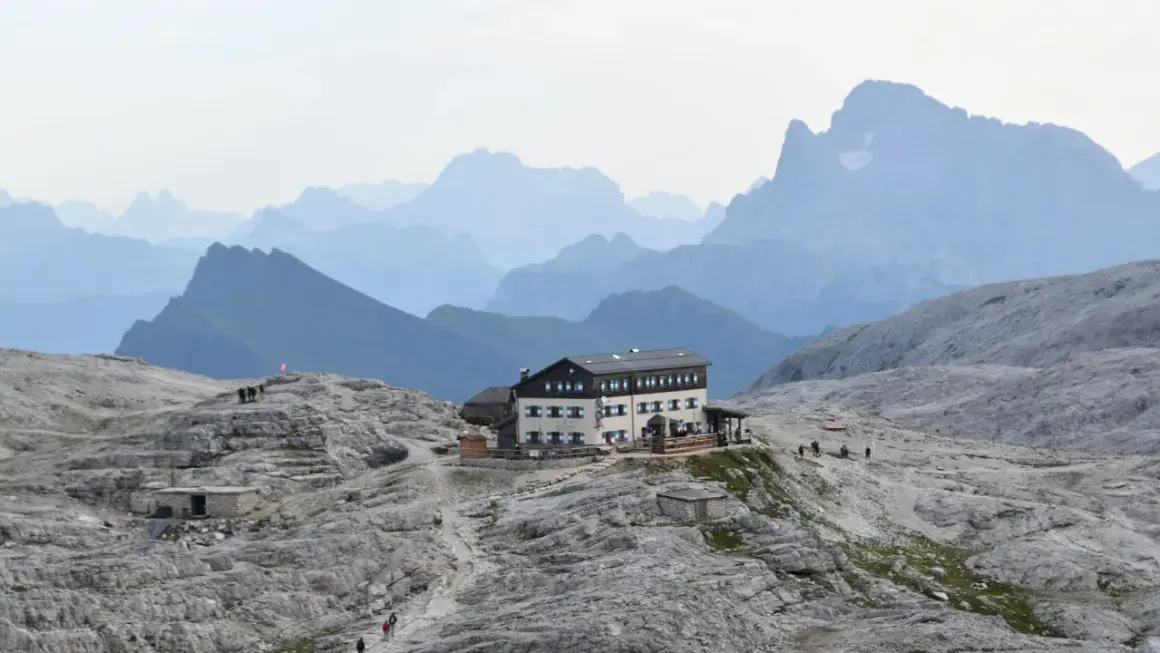 Il rifugio Rosetta, un edificio imponente, si erge su un terreno roccioso con montagne sfumate all'orizzonte.