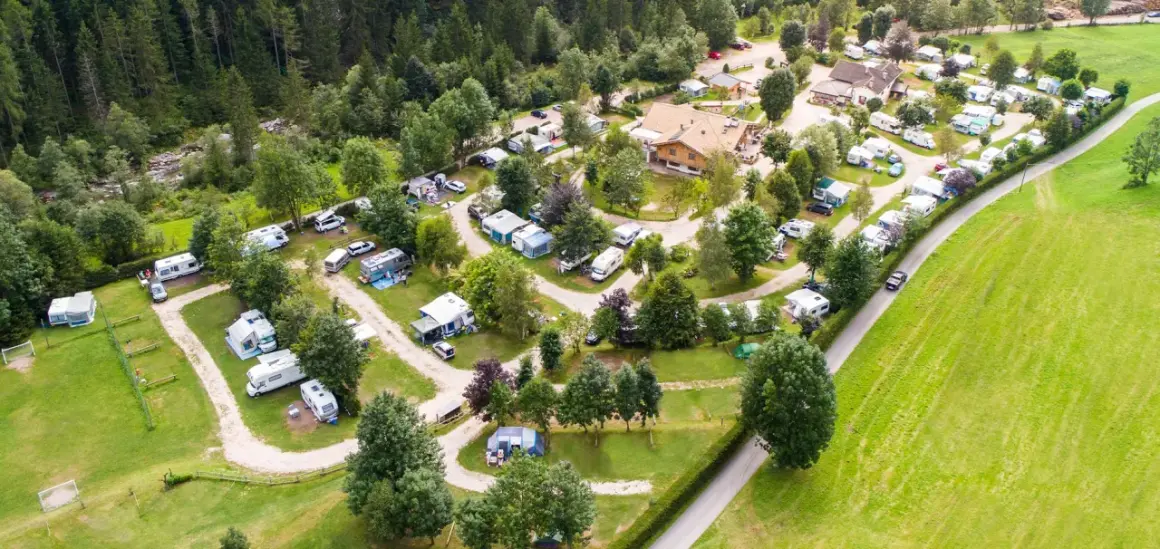 Vista aerea di un campeggio immerso nel verde, con roulotte, camper e tende disposti su prati e sentieri. Un luogo ideale per una vacanza in **camping valle verde**.