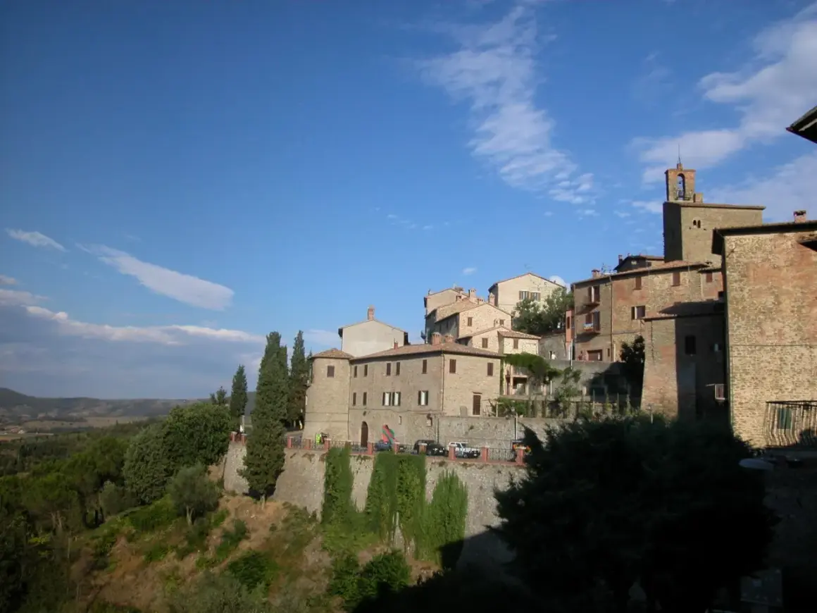 Borgo medievale di Panicale, Perugia, con case in pietra e mattoni, cipressi e vista sulla campagna umbra sotto un cielo azzurro.