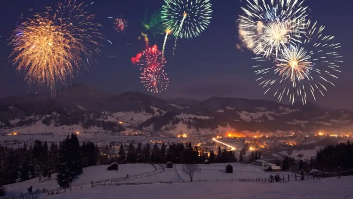 Fuochi d'artificio colorati illuminano il cielo notturno sopra un villaggio innevato, celebrando il capodanno in montagna.