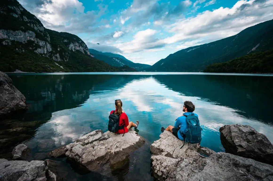 Coppia ammira il **lago di Molveno** da rocce, circondati da montagne verdi e cielo azzurro con nuvole bianche.