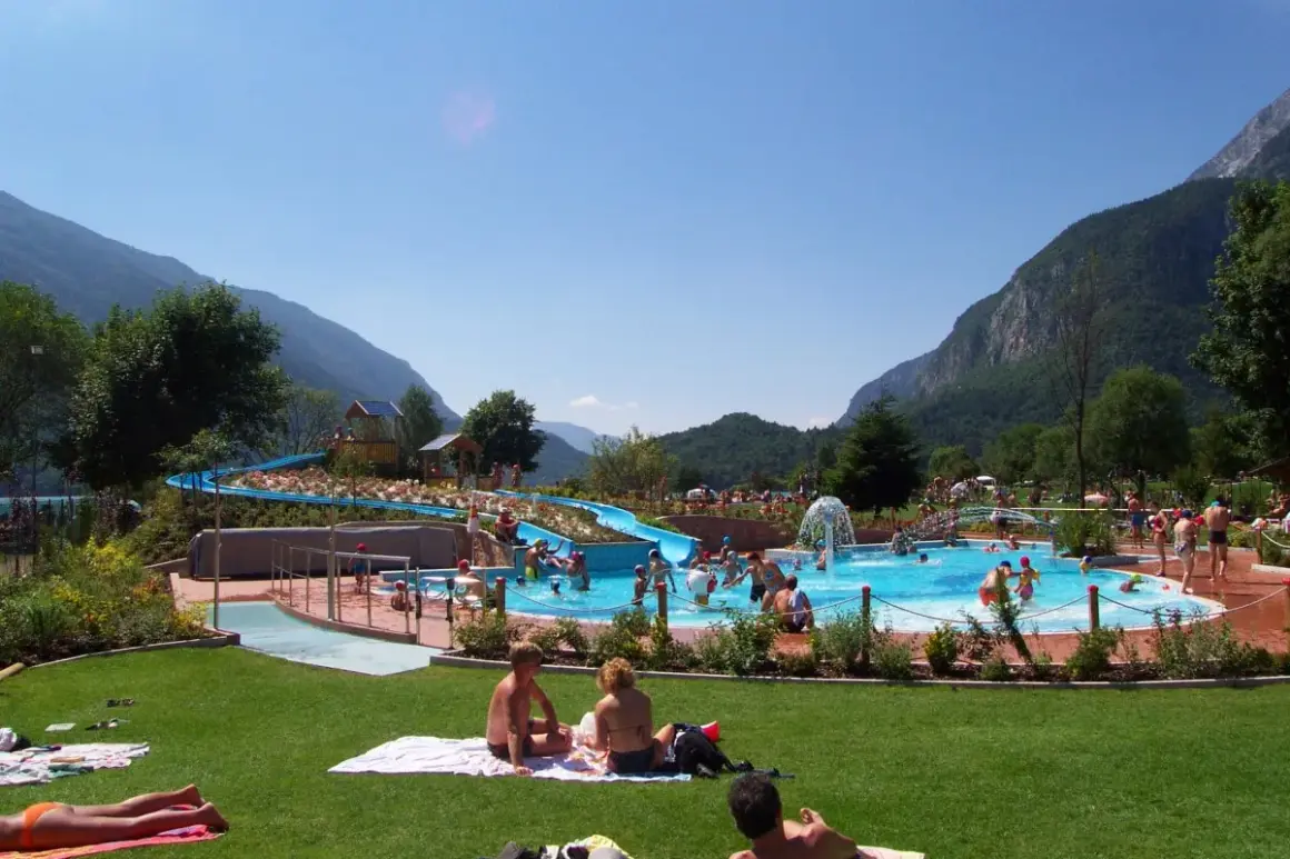 Giornata di sole all'acquapark Molveno, con scivoli blu, piscine piene di gente e montagne sullo sfondo.
