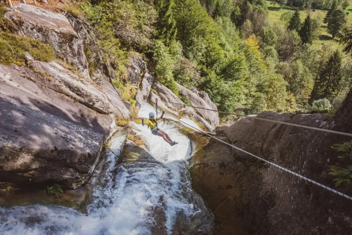 Donna in zipline sopra una cascata nella Val Daone, con rocce e alberi circostanti.