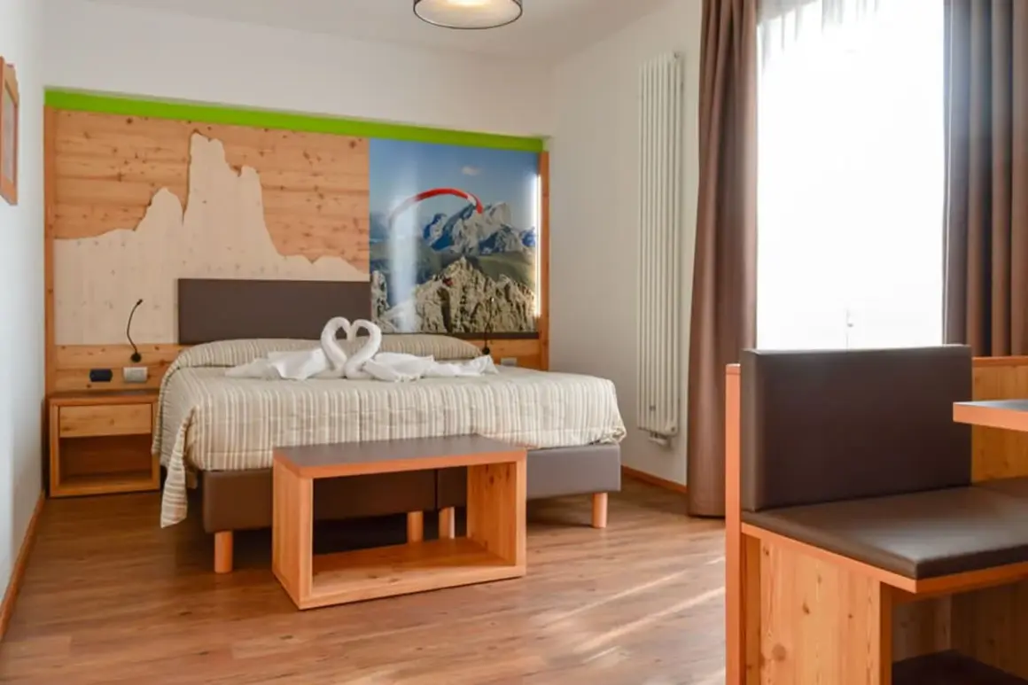 Camera accogliente con letto decorato da cigni in asciugamano, testiera in legno con panorama montano, tipica del hotel panorama wellness & resort***s.
