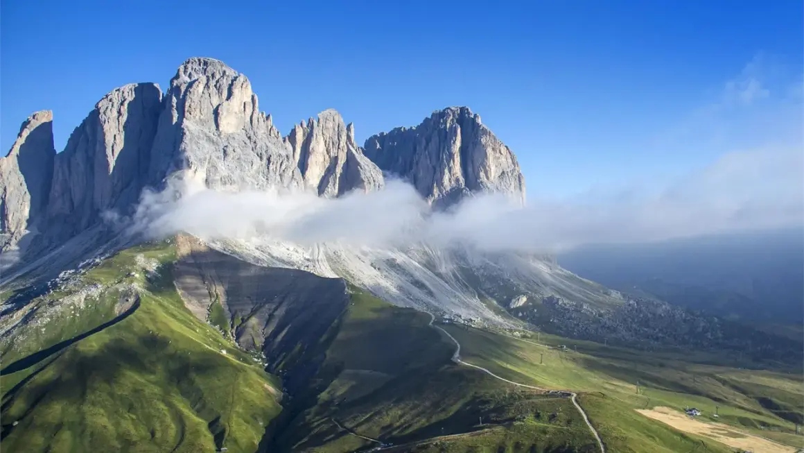 Vette maestose delle Dolomiti avvolte da nuvole, con un sentiero che sale verso il rifugio Col Rodella.