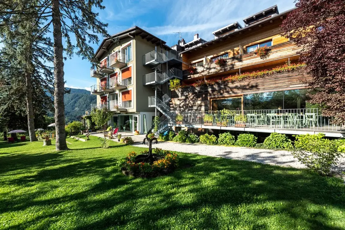 Il la roccia wellness hotel, con la sua facciata in legno e le terrazze fiorite, si affaccia su un prato verde curato, invitando al relax.