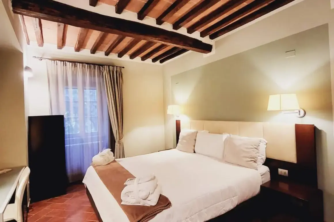 Camera accogliente con soffitto a travi in legno, letto king-size e accappatoi pronti per il relax al Cortona Resort e Spa.