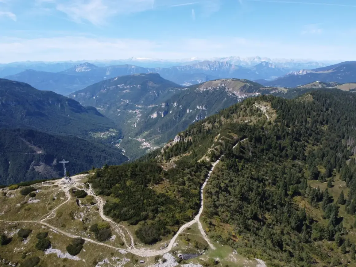 Sentiero che sale verso la croce sul monte Maggio, con vista su valli verdi e montagne all'orizzonte.