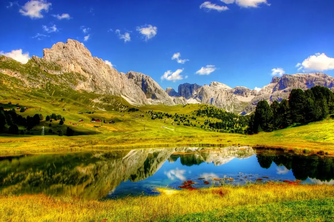 Un lago alpino riflette montagne maestose e prati verdi. Perfetto per le cose da fare in estate: escursioni, relax e ammirare la natura.