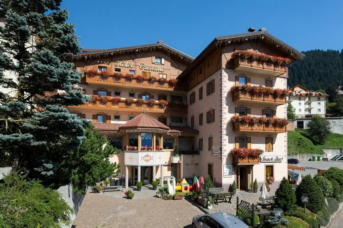 Hotel Andalo, un edificio alpino con balconi fioriti e un'area giochi per bambini, immerso nel verde.