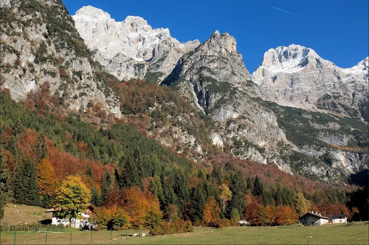 Malga Movlina, un rifugio alpino immerso nel foliage autunnale, con montagne imponenti sullo sfondo e un cielo azzurro limpido.