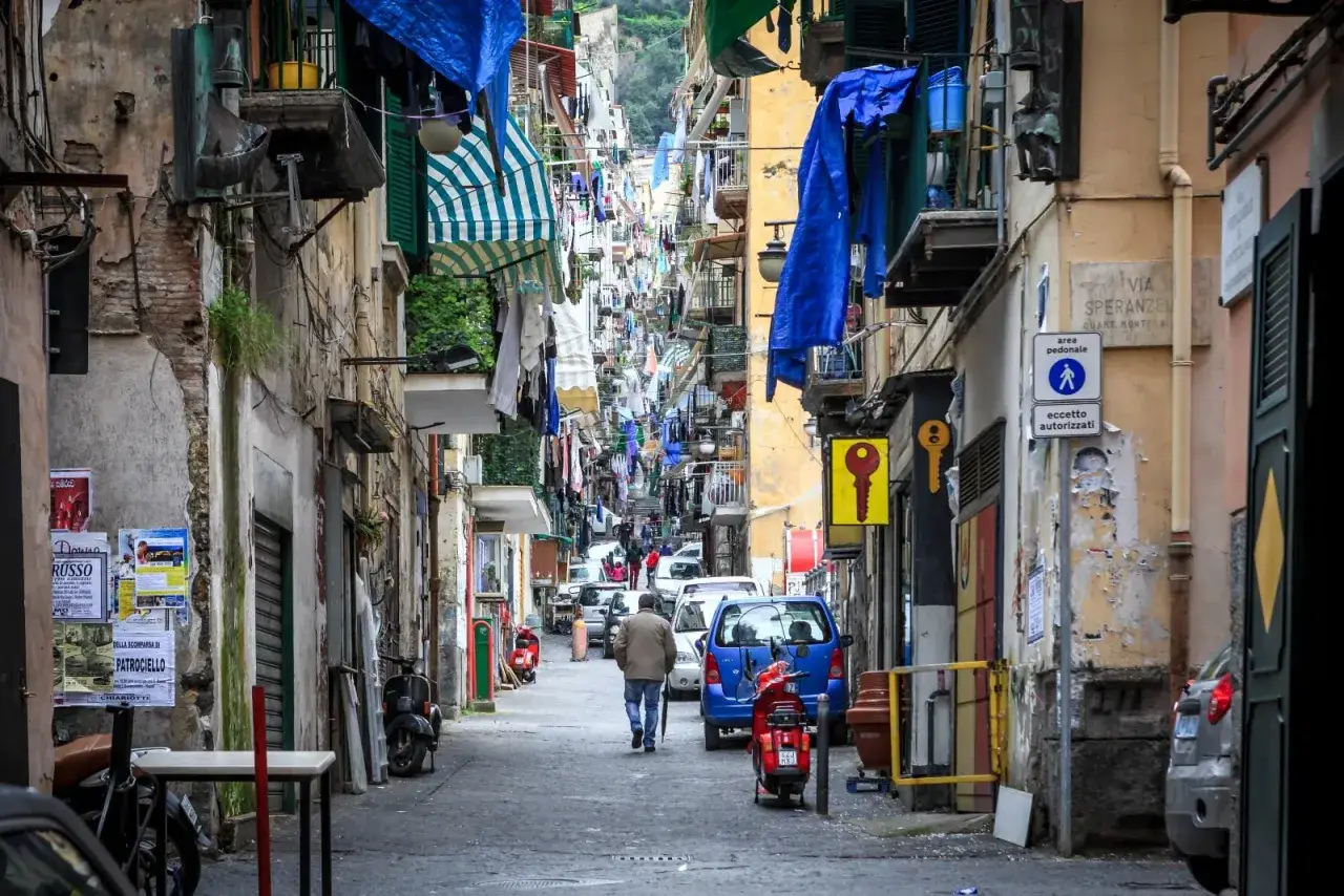 Un vicolo stretto a Napoli, pieno di panni stesi, scooter e auto. Un vero scorcio autentico, tra i tanti posti da visitare a Napoli.