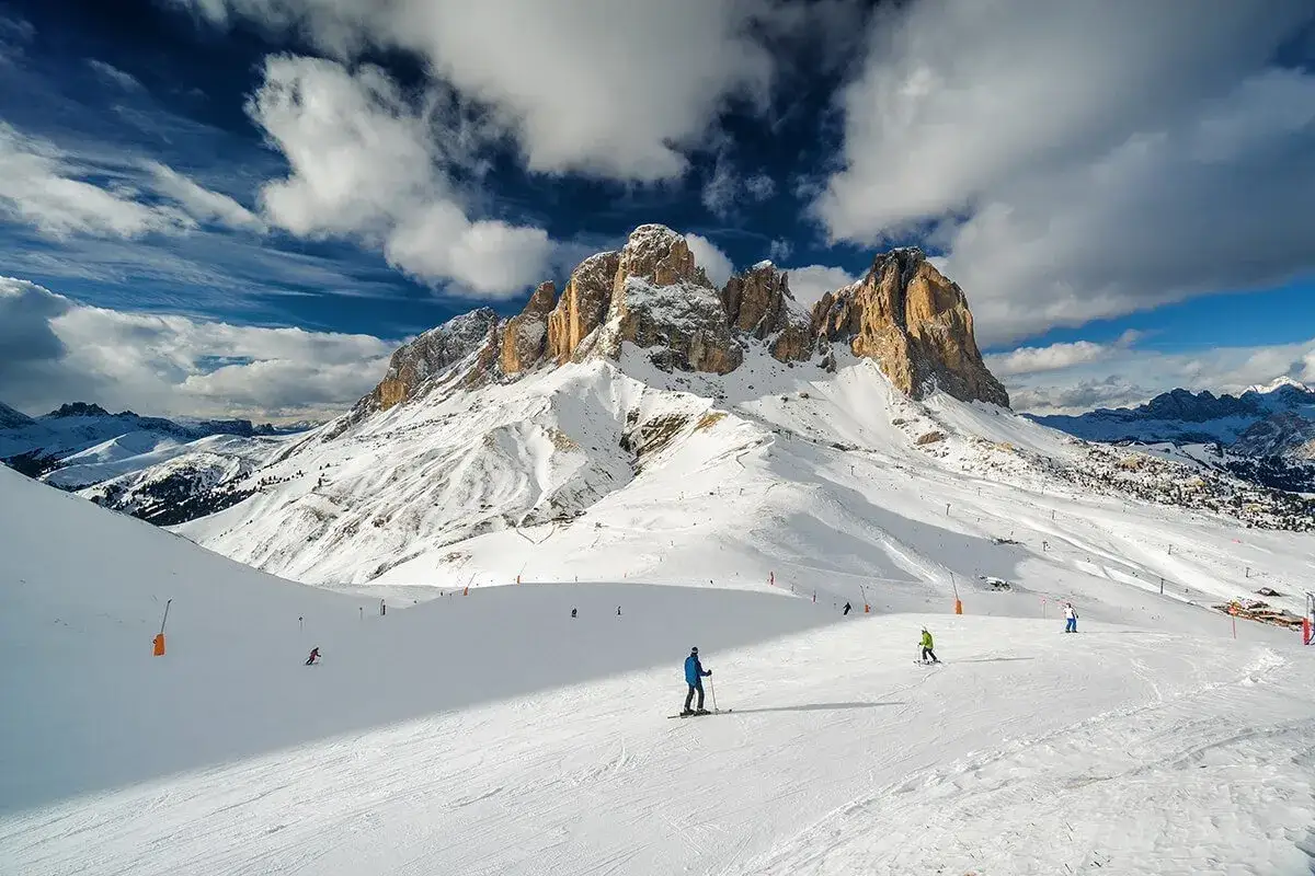 Piste innevate a Canazei, con sciatori che scendono sotto maestose vette dolomitiche. Un perfetto scenario di canazei inverno.