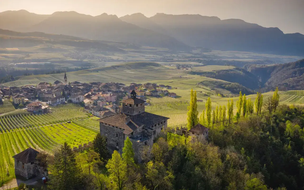 Un borgo pittoresco nel Val di Non, con un castello in primo piano, vigneti rigogliosi e montagne sullo sfondo.
