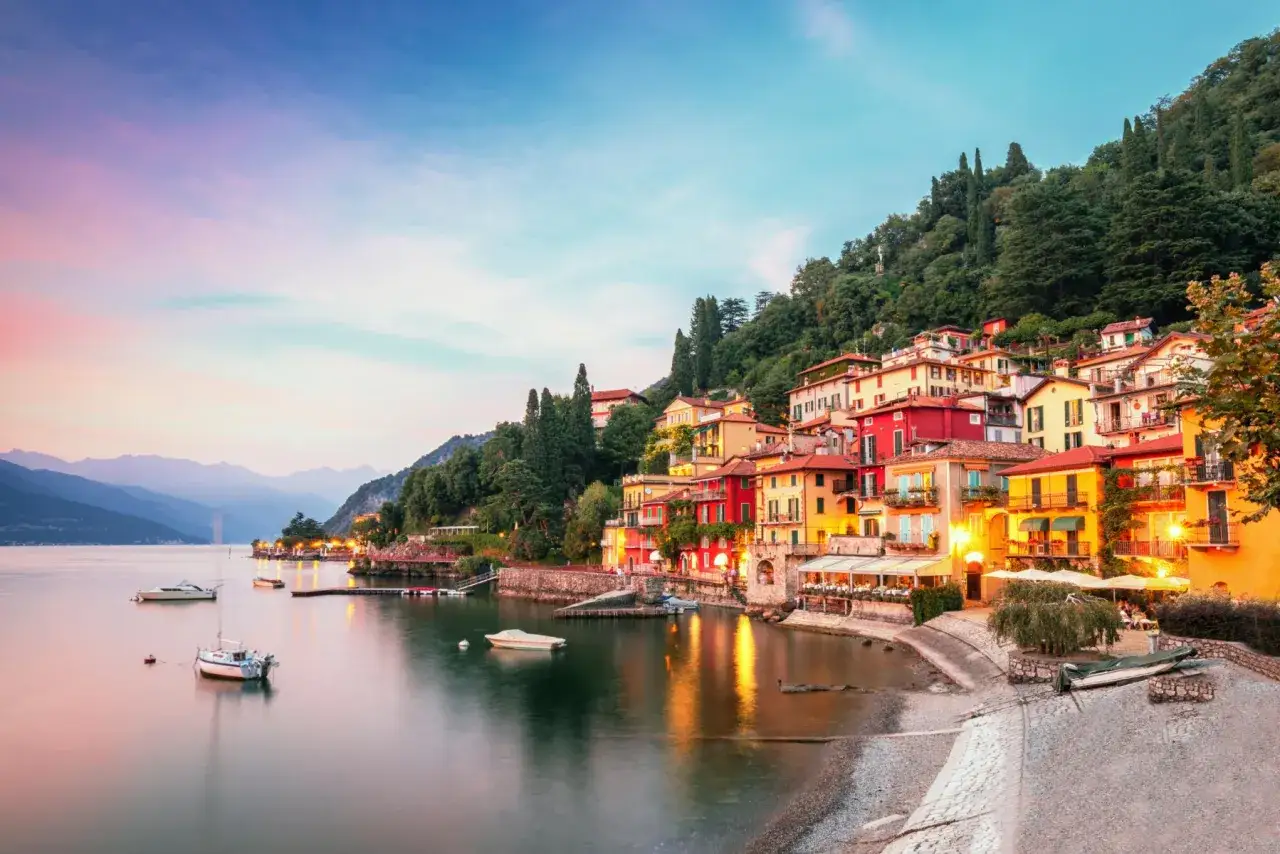 Colorate case affacciate sul lago, un sogno per le vacanze al lago. Barche ormeggiate e montagne sullo sfondo.