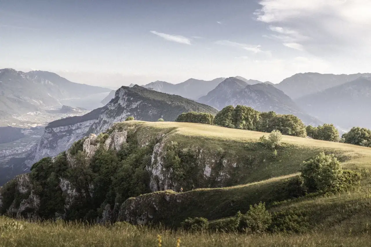 Due escursionisti camminano sul crinale erboso del Monte Casale, con montagne sfumate all'orizzonte.