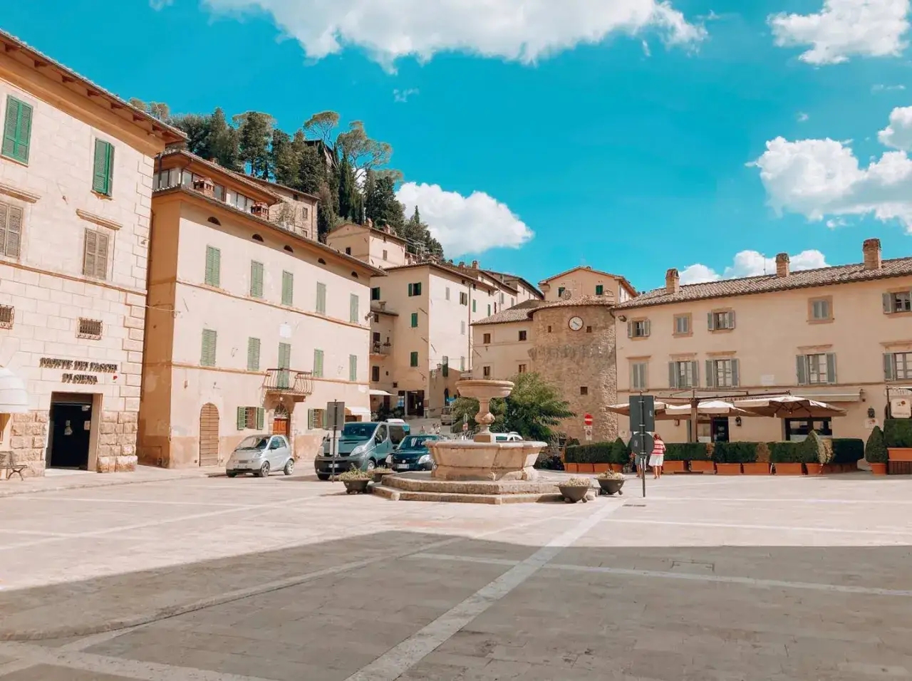 Piazza di Cetona: cosa vedere? Una fontana storica, palazzi color crema e un cielo azzurro con nuvole bianche.