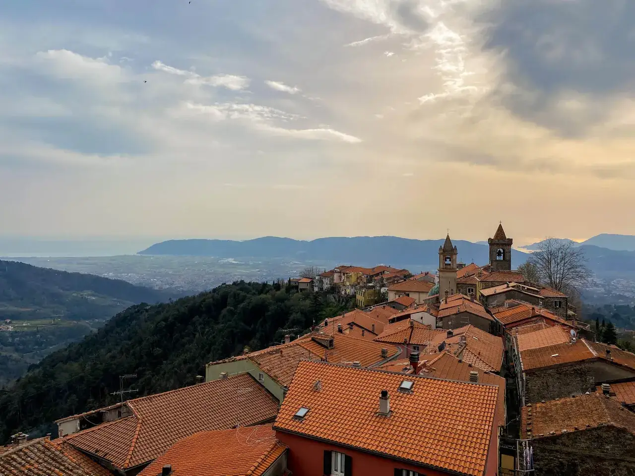 Panoramica di un borgo con tetti rossi, dove si trova Fosdinovo, incastonato tra colline verdi e il mare all'orizzonte.