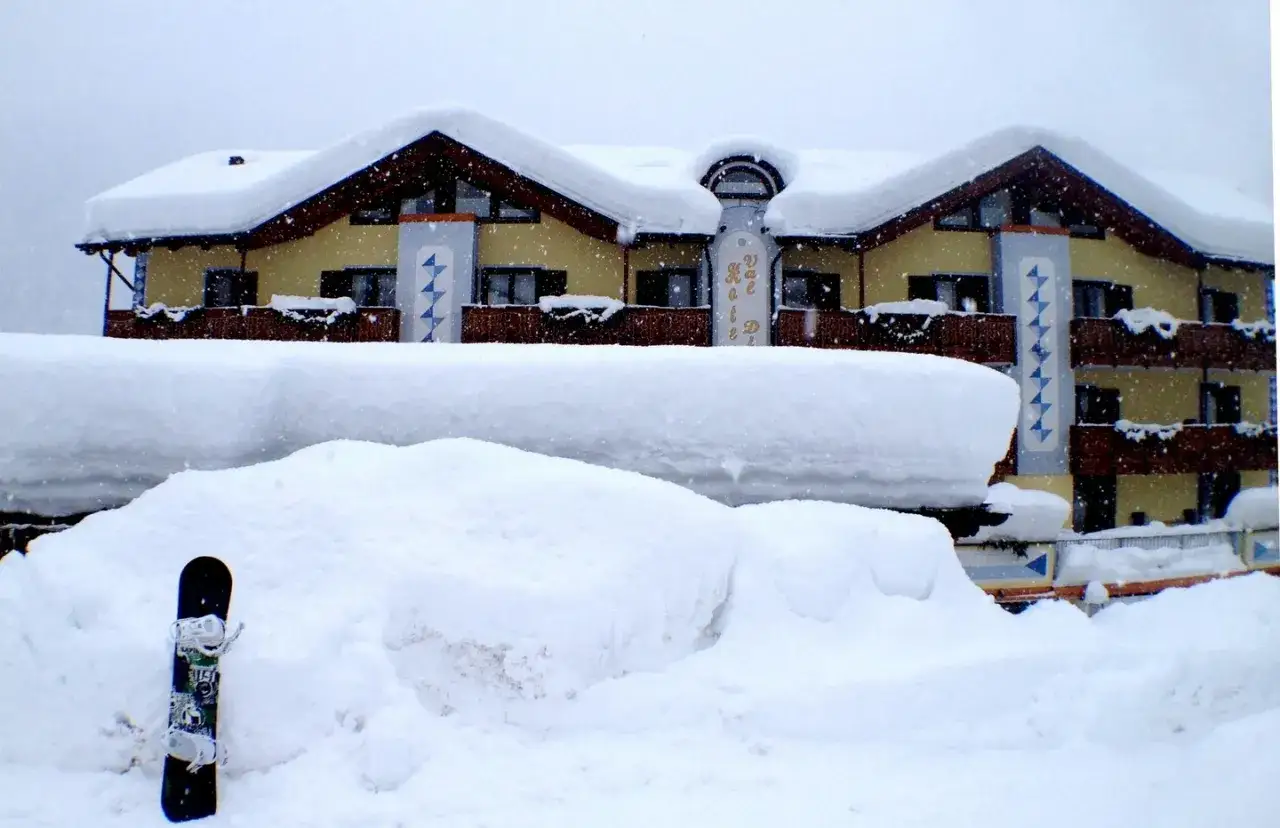 Un hotel innevato in Val di Sole, con uno snowboard piantato nella neve.