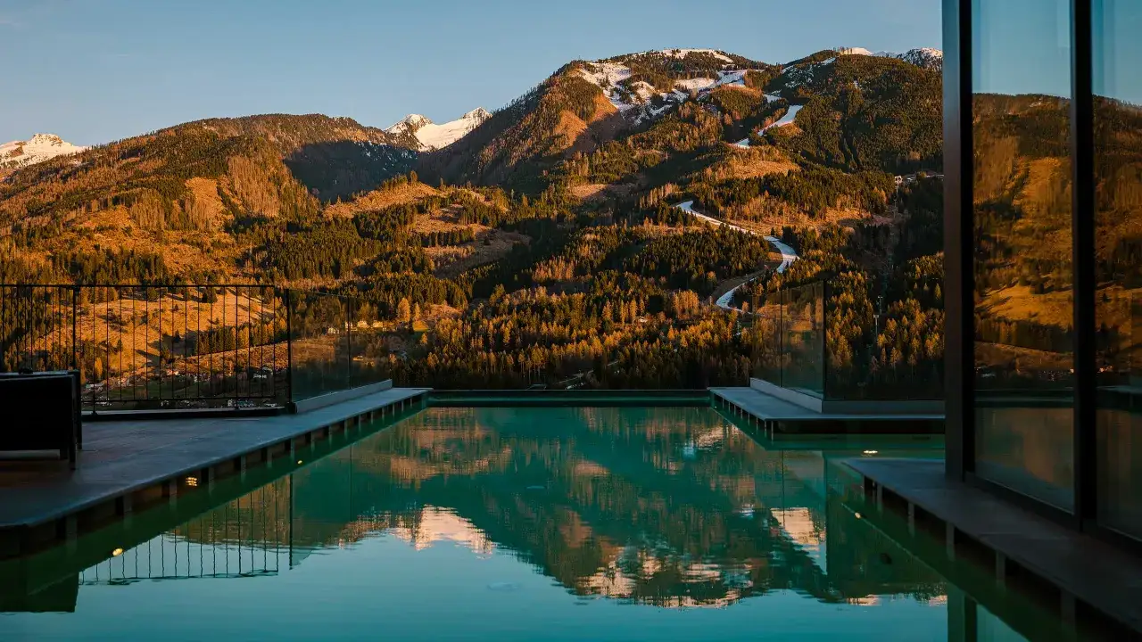 Piscina a sfioro con vista sulle montagne innevate e boschi dorati, riflessi sull'acqua. Un'oasi di pace al la roccia wellness hotel.