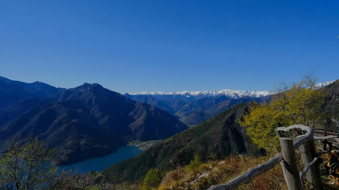 Vista panoramica del lago di Ledro con montagne innevate all'orizzonte e un recinto in legno in primo piano.