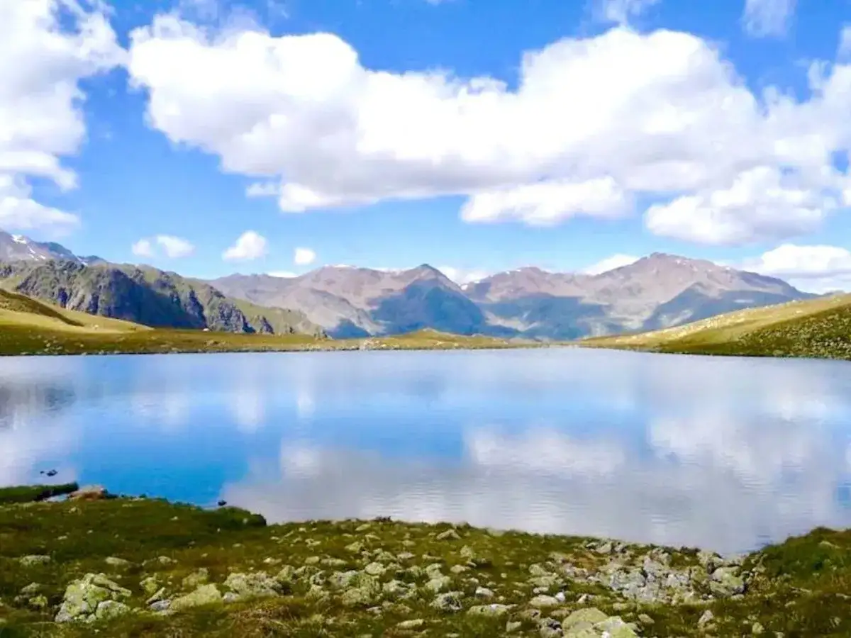 Un sereno lago alpino riflette il cielo azzurro e le montagne circostanti. Un paesaggio da sogno nel cuore del lago trenta.