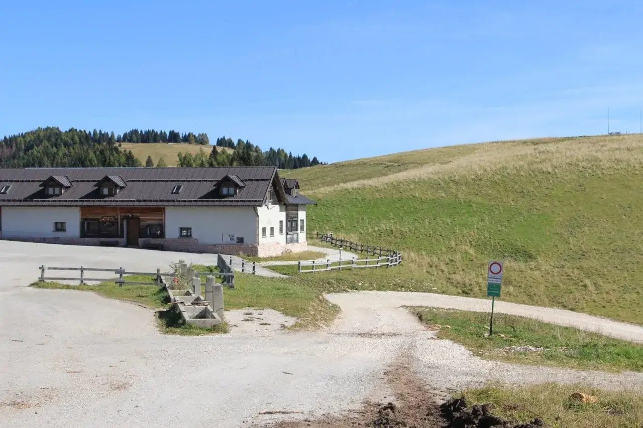 Malga Arpaco, un edificio bianco con tetto scuro, si erge su un prato verde sotto un cielo azzurro.