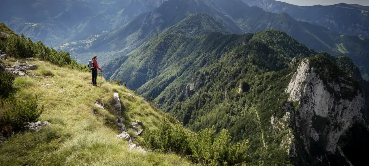 Escursionista ammira il panorama mozzafiato dal Monte Zugna, circondato da verdi montagne e valli profonde.