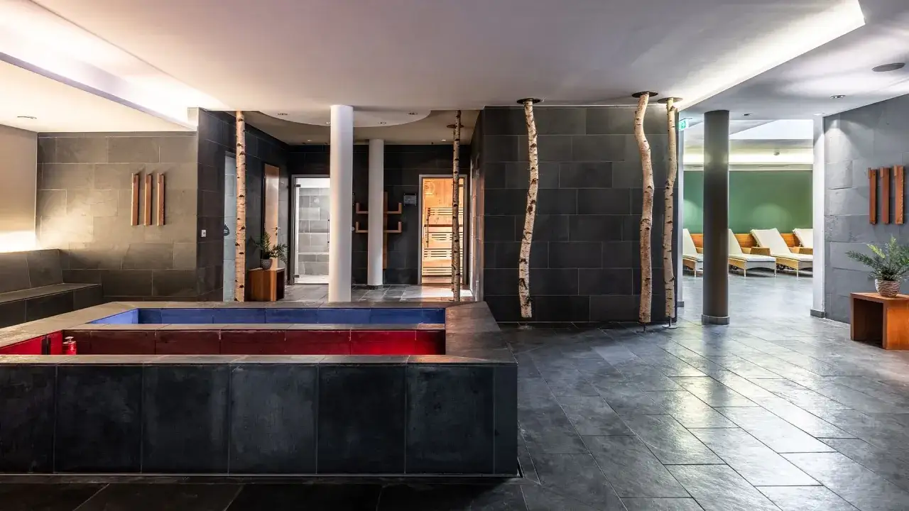 Area benessere del Falkensteiner Hotel Antholz: vasca idromassaggio con luci rosse e blu, sauna in legno e lettini relax.
