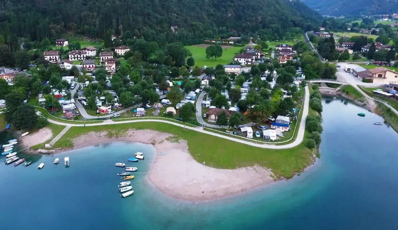 Villaggio vacanze con case e tende, vicino al lago azzurro di Ledro. Barche ormeggiate sulla riva.