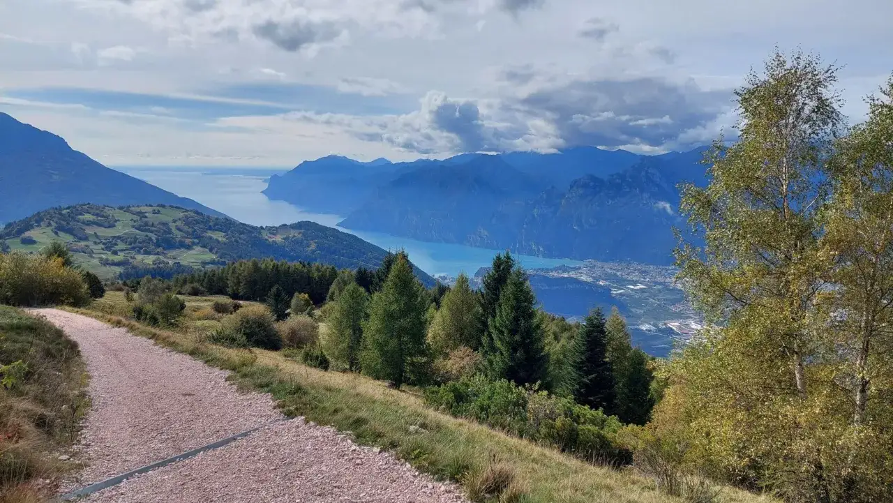 Sentiero sterrato che porta verso il passo Bordala, con vista su un lago azzurro e montagne blu.