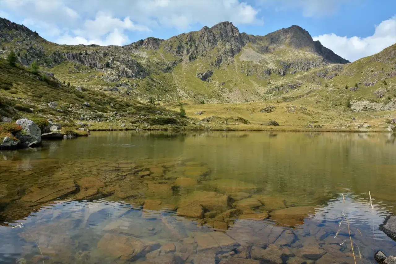 Lago alpino cristallino con rocce sommerse, circondato da verdi pendii e montagne imponenti. Un luogo sereno vicino alla malga Vallazza.