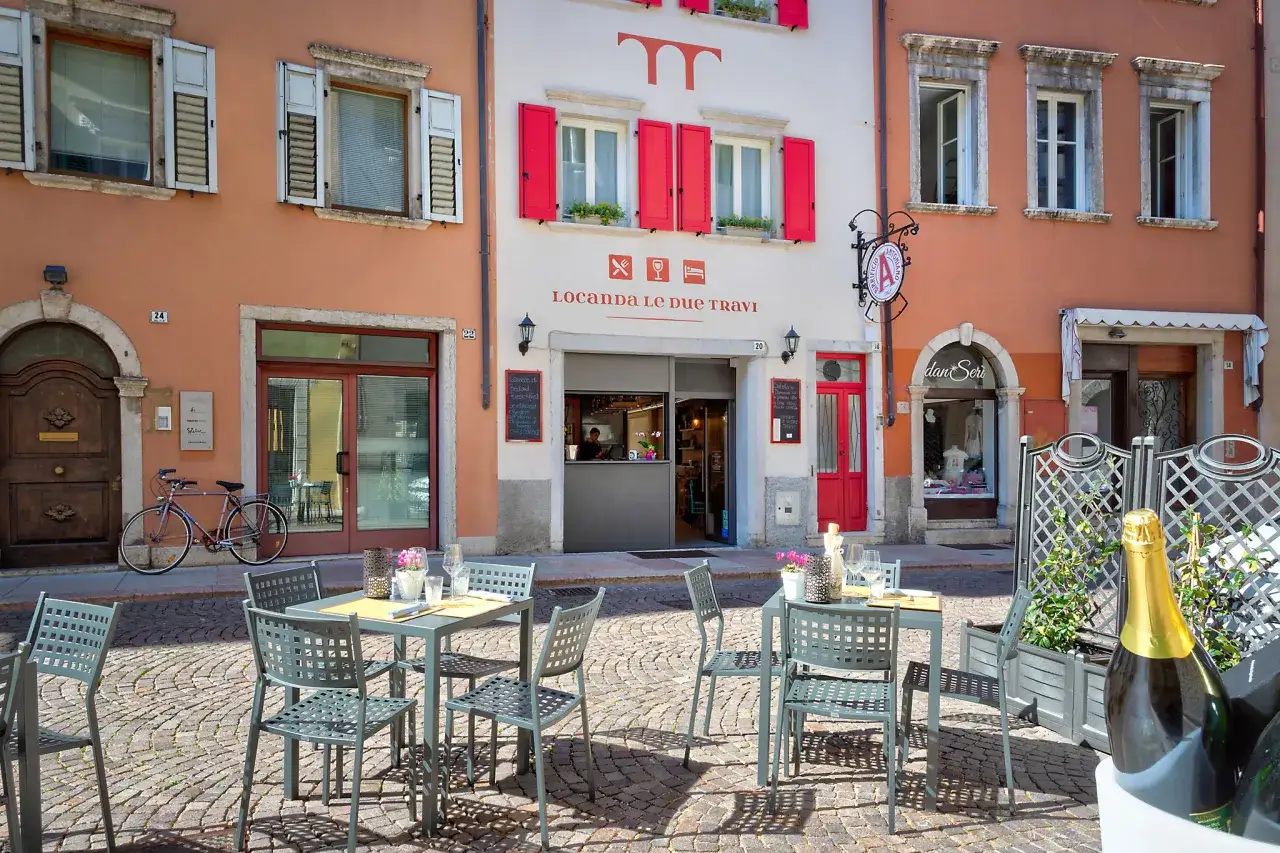 Tavoli all'aperto della Locanda Le Due Travi a Trento, con un'atmosfera invitante e una bottiglia di spumante pronta per essere gustata.