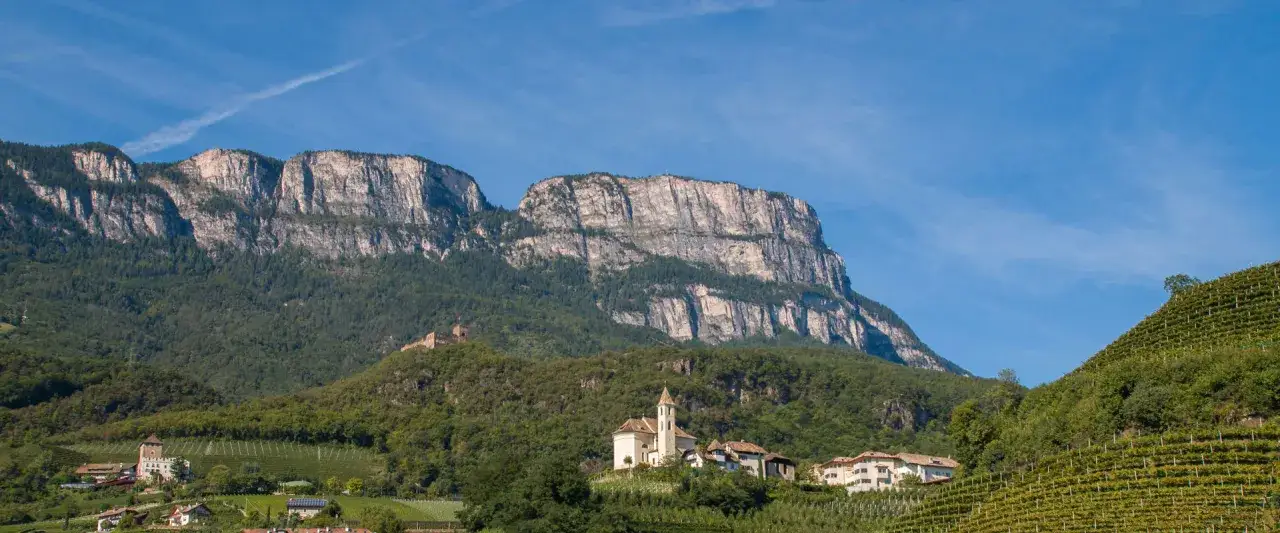 Imponente monte Macaion con vigneti terrazzati e un borgo con chiesa.