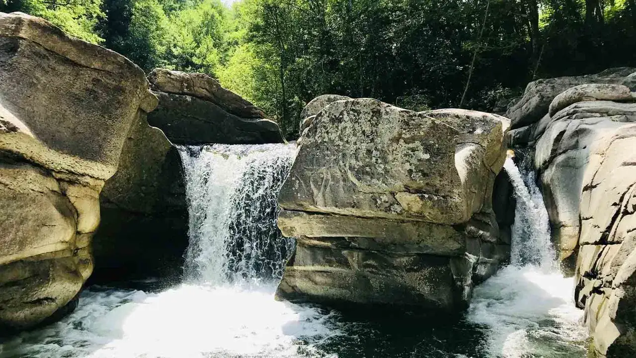 Cascate naturali nel Val di Farma, con rocce levigate dall'acqua e vegetazione lussureggiante.