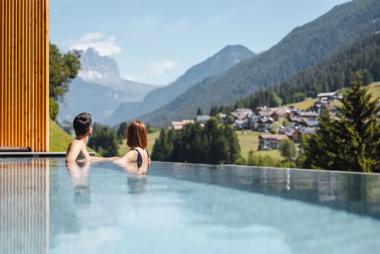 Coppia rilassata in piscina con vista panoramica sulle Dolomiti. Un'esperienza di puro benessere in un wellness hotel Dolomia.